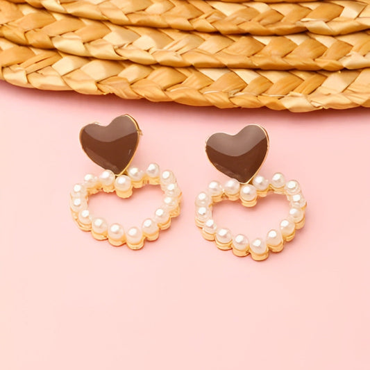 Heart-shaped earrings with pearl detailing on a pink background
